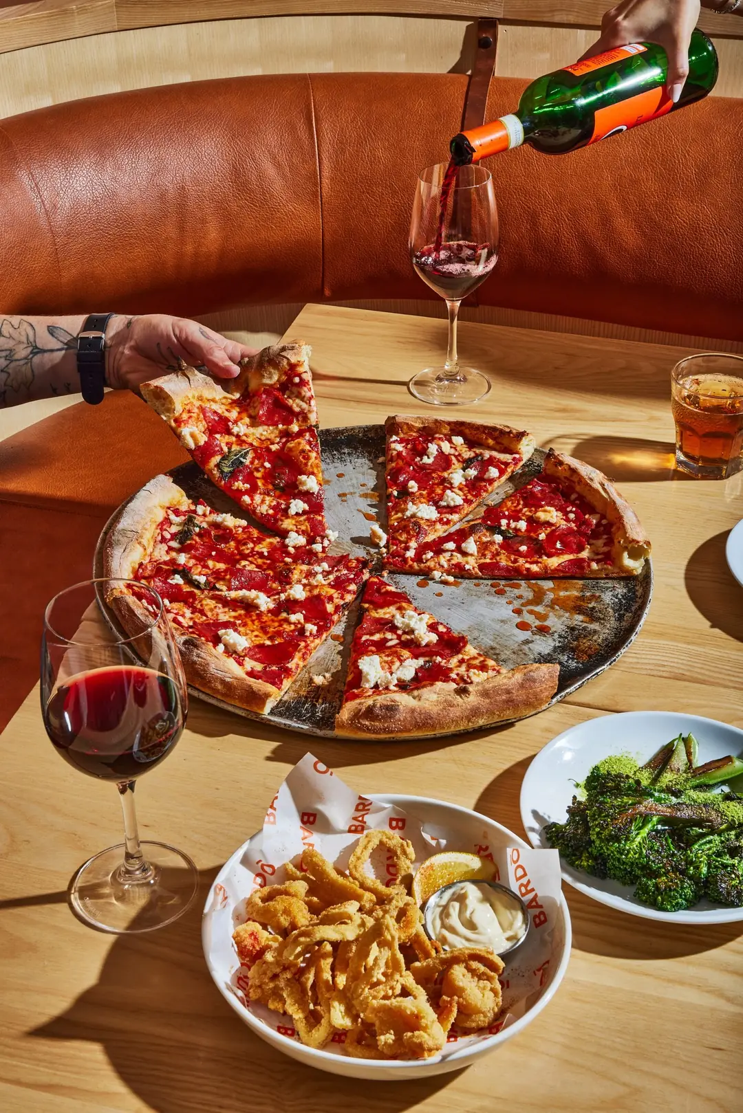 A hand pulling a slice from a stone-baked pizza at Bardō