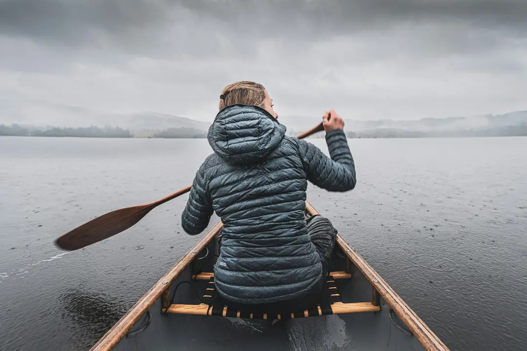 A woman paddling a canoe across a still, misty lake