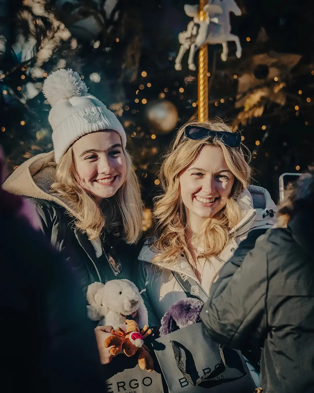 Two friends in toques smiling at the Distillery Winter Village at night