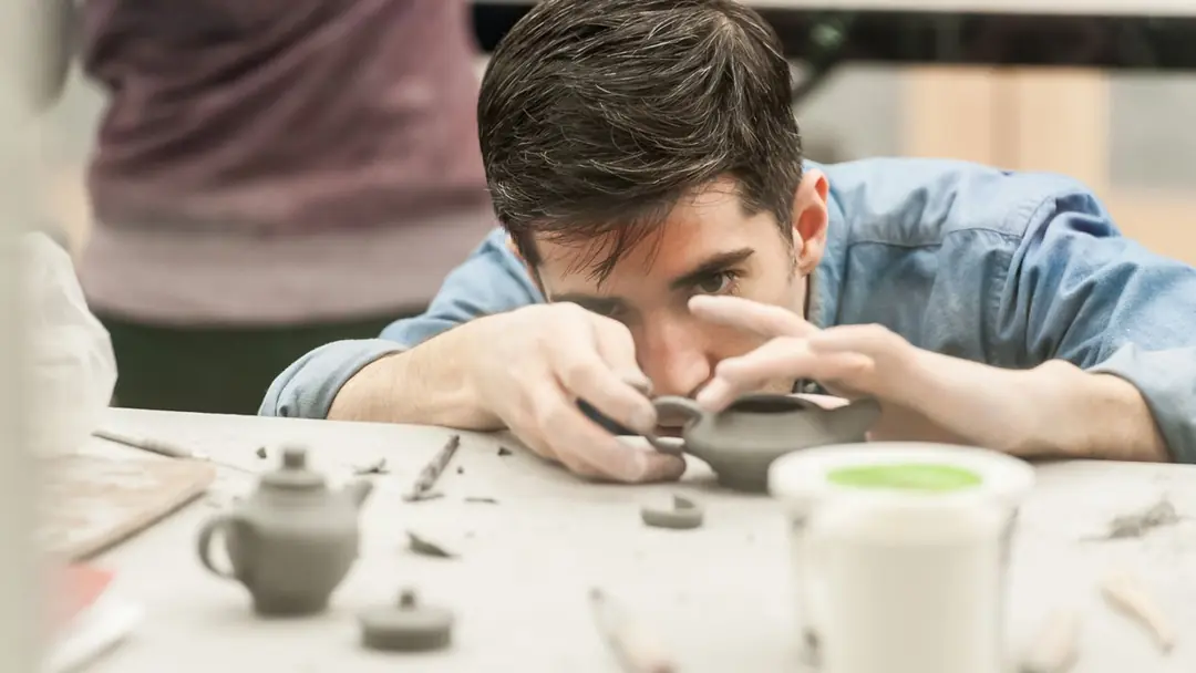 A man carefully shaping a small clay teapot in the Gardiner Museum studio