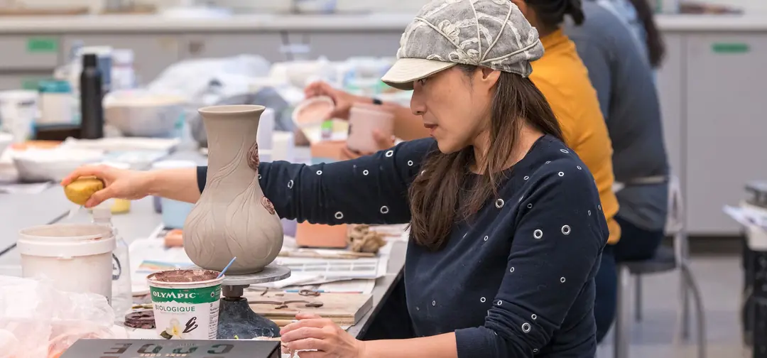 A student shaping a clay vase in a Gardiner Museum clay class