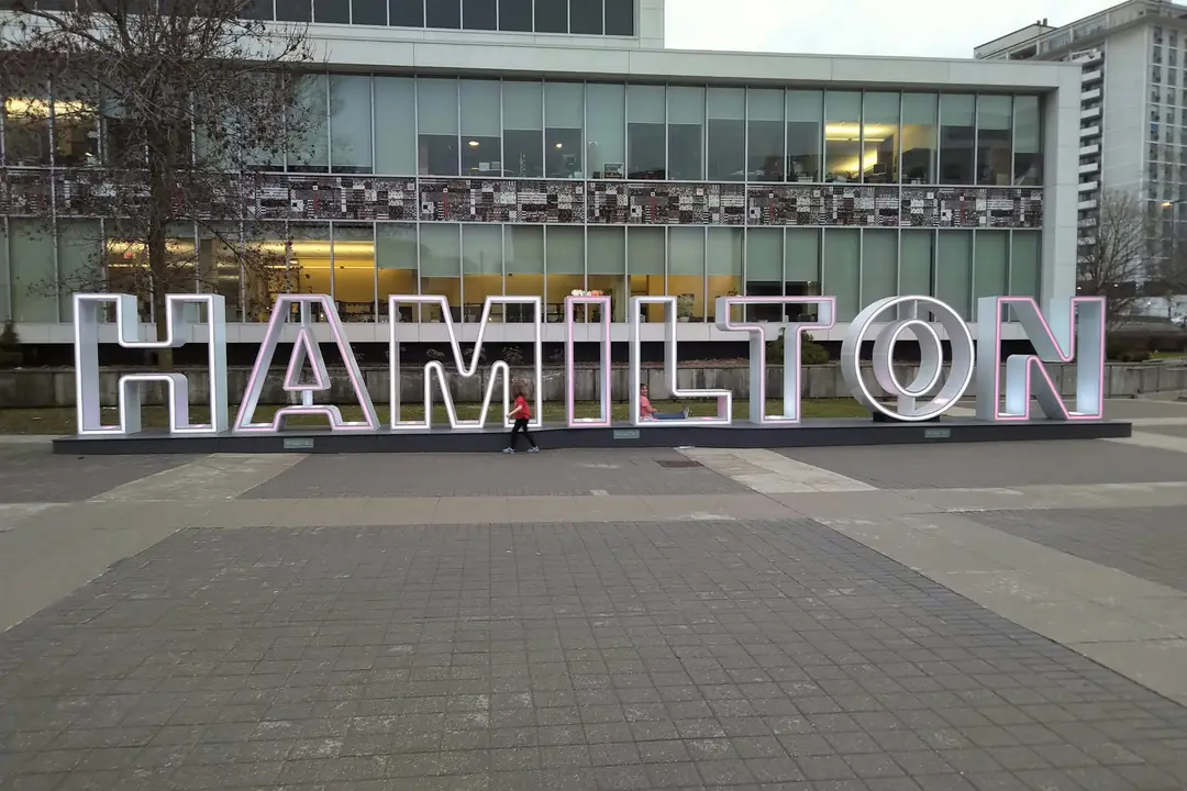 People walking past the big HAMILTON letters outside Hamilton City Hall