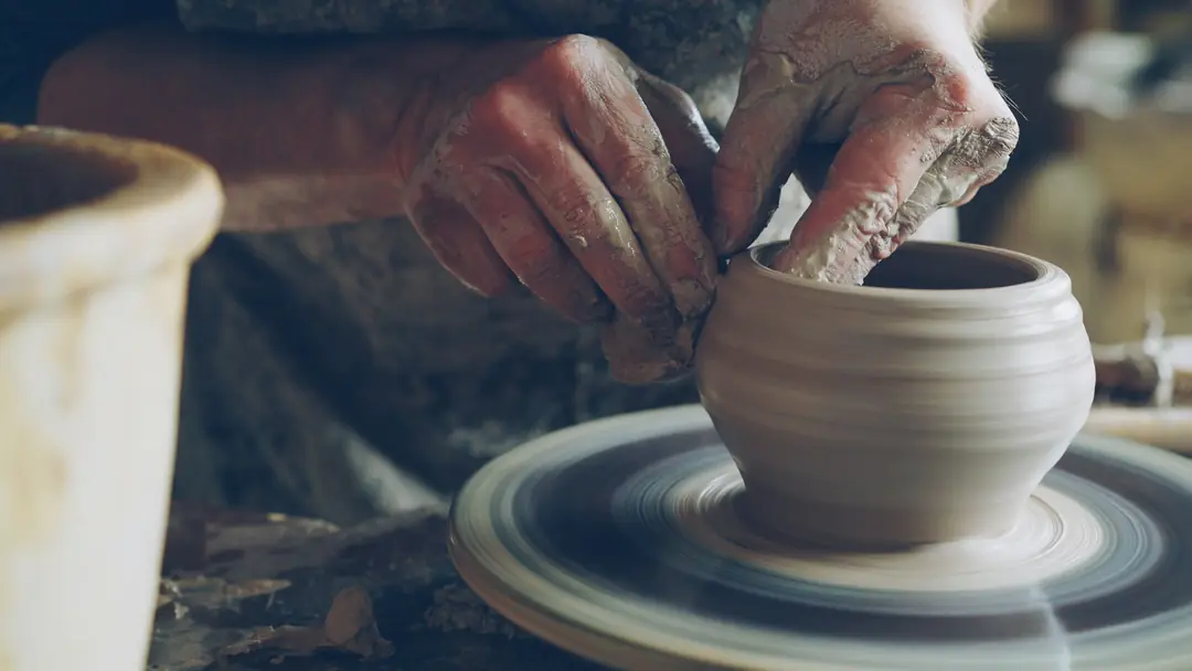 Hands shaping a clay pot on a spinning pottery wheel