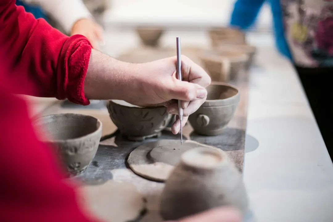 A pottery class in progress, shaping and carving small clay cups at a long table